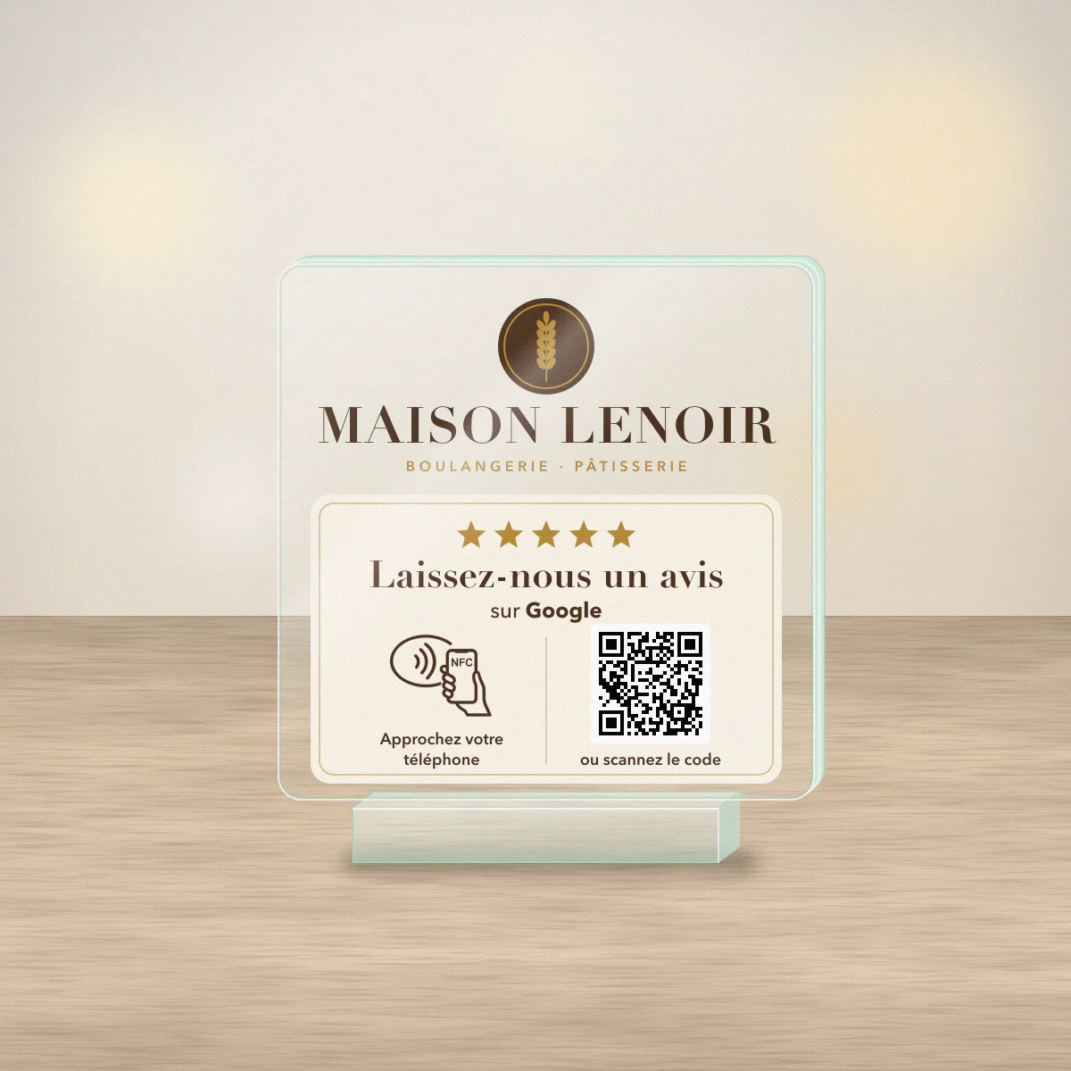 Plaque avis Google en plexiglas transparent posée sur le comptoir d’une boulangerie, imprimée en couleur au logo de l’enseigne fictive Maison Lenoir, avec QR code et puce NFC